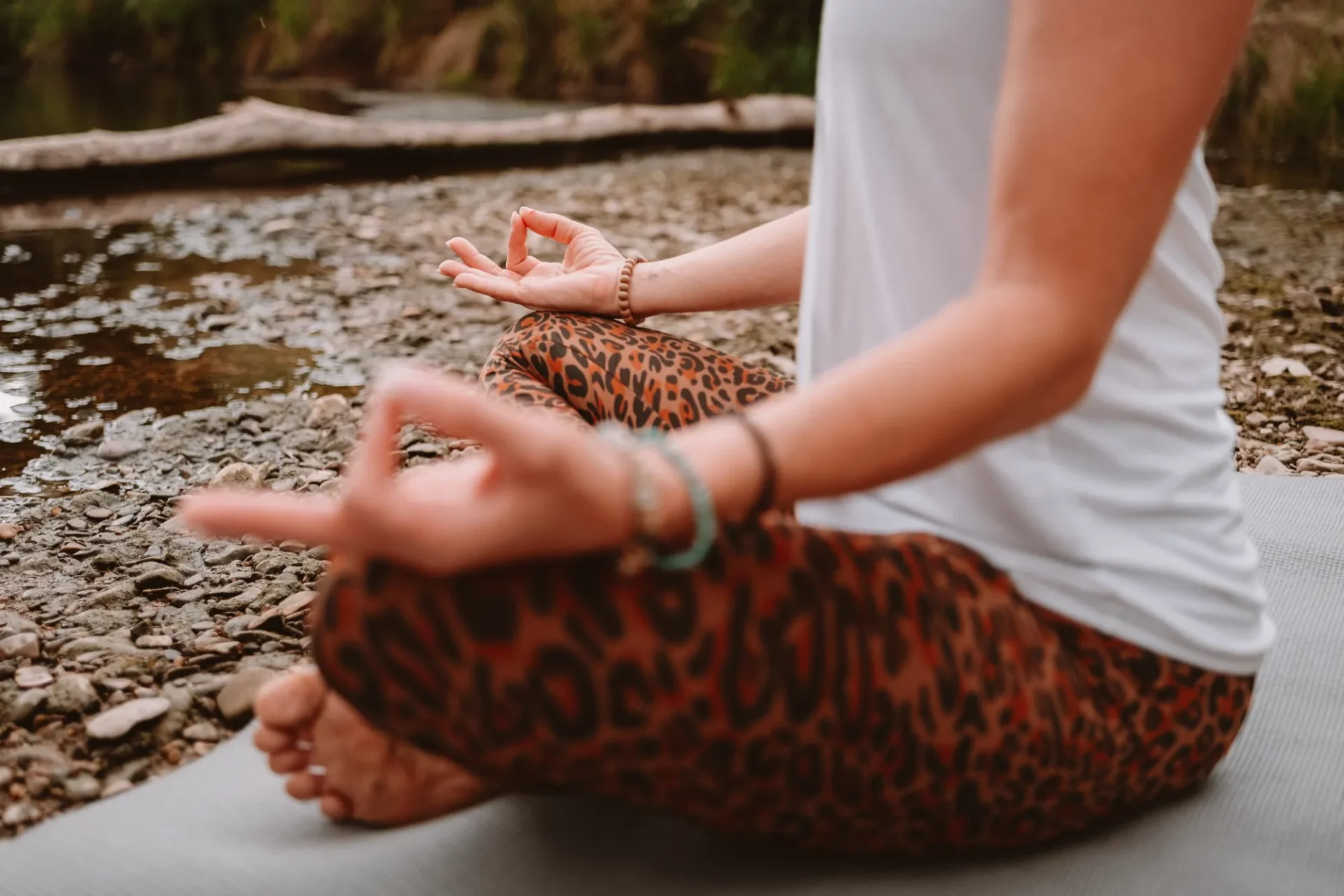 Hände in Meditationshaltung, im Schneidersitz auf der Matte am Flussufer