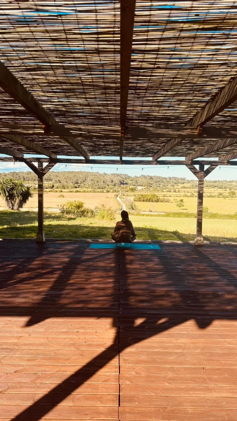 Meditation auf einer überdachten Holzterrasse mit Blick über weite Felder