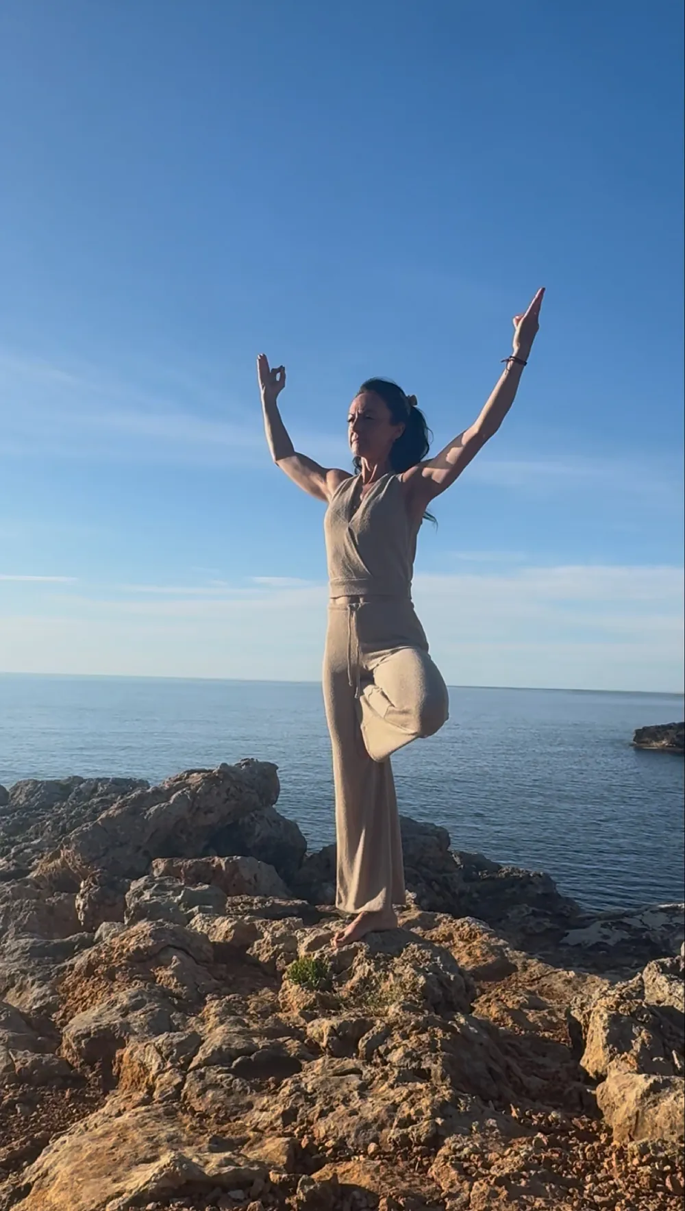 Yogalehrerin im Baum mit erhobenen Armen auf einem Felsen am Meer