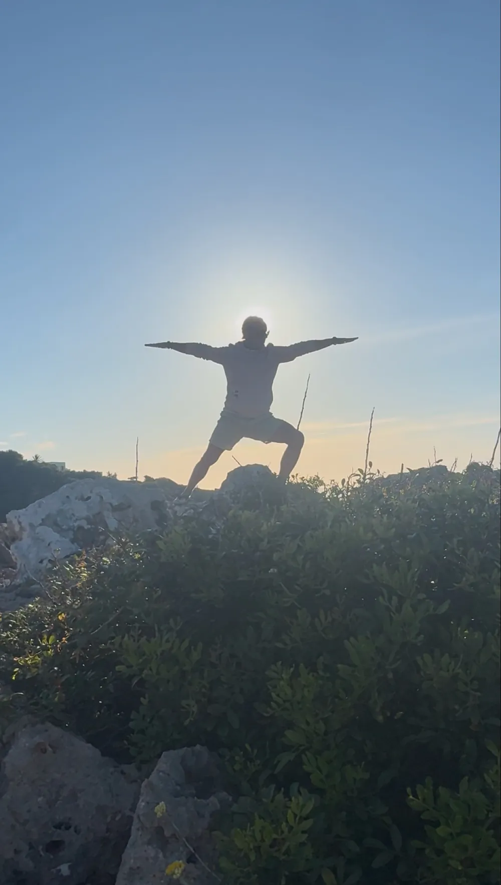 Yogapose mit ausgebreiteten Armen im Gegenlicht auf einem Felsen