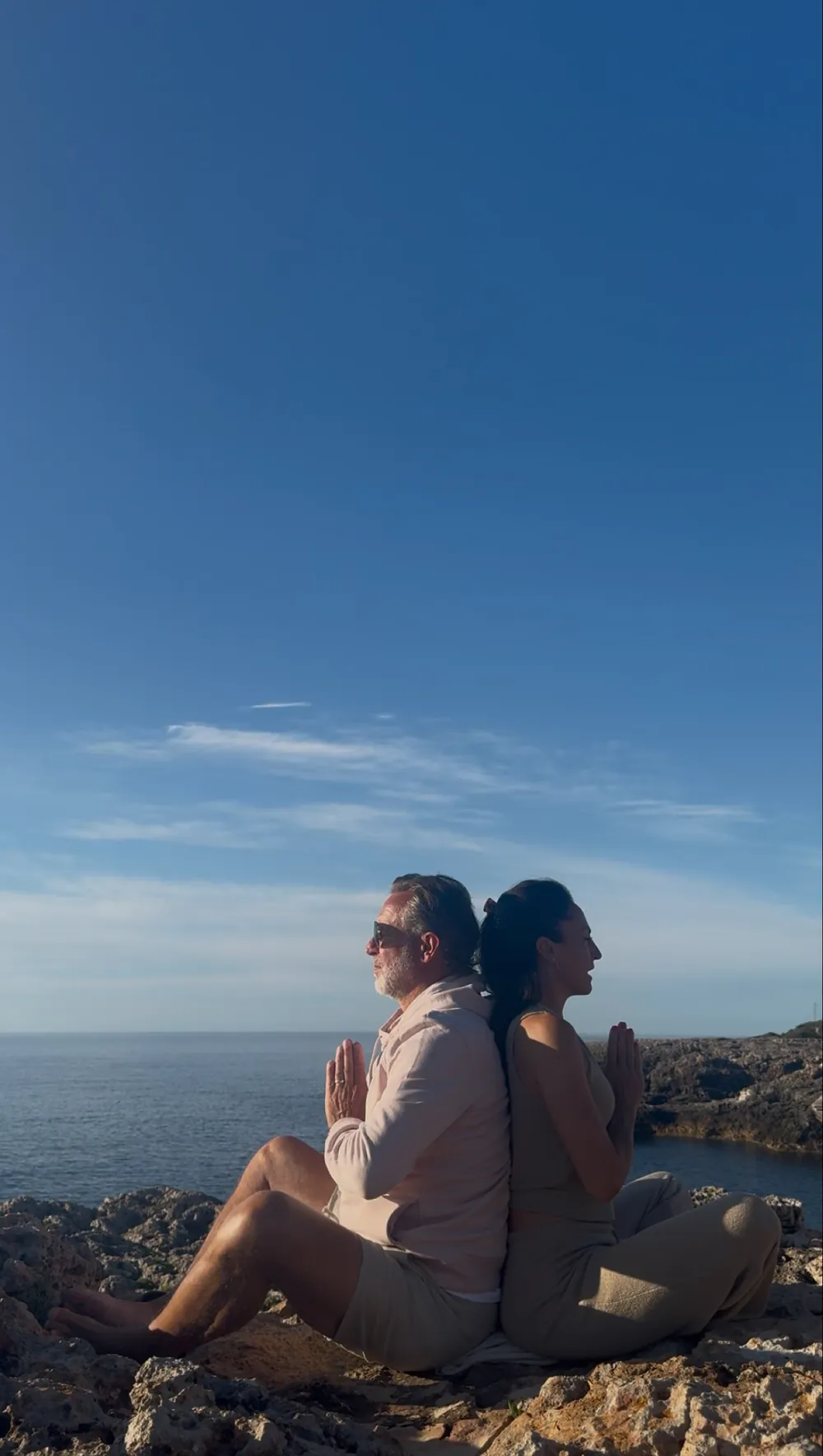 Birgit und Dirk sitzen Rücken an Rücken in Meditation auf den Klippen über dem Meer