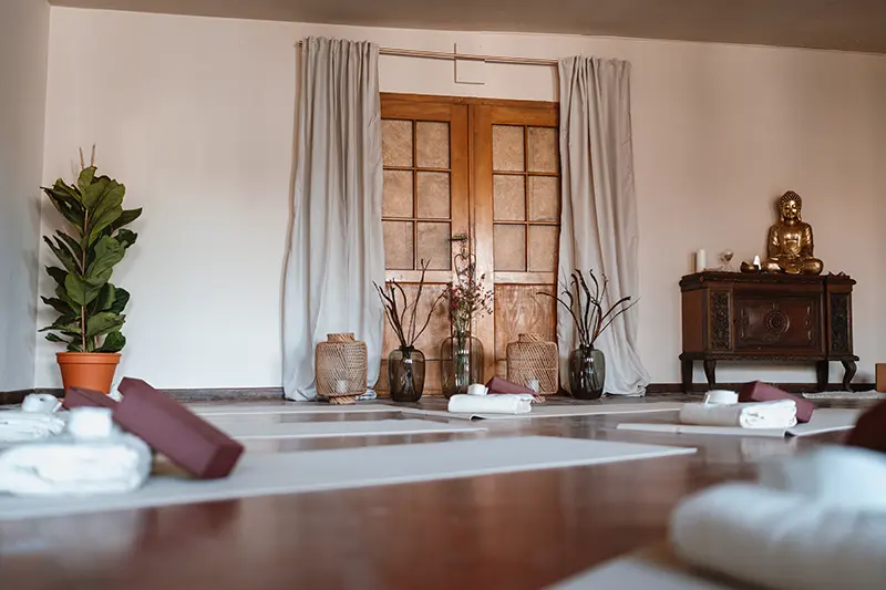 Weiter Kursraum bei inside. mit ausgelegten Matten, Pflanze und Buddhafigur